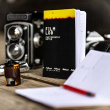 Film Log Photography Notes sits among a Rolleiflex camera, a roll of 35mm film, and a roll of 120 film