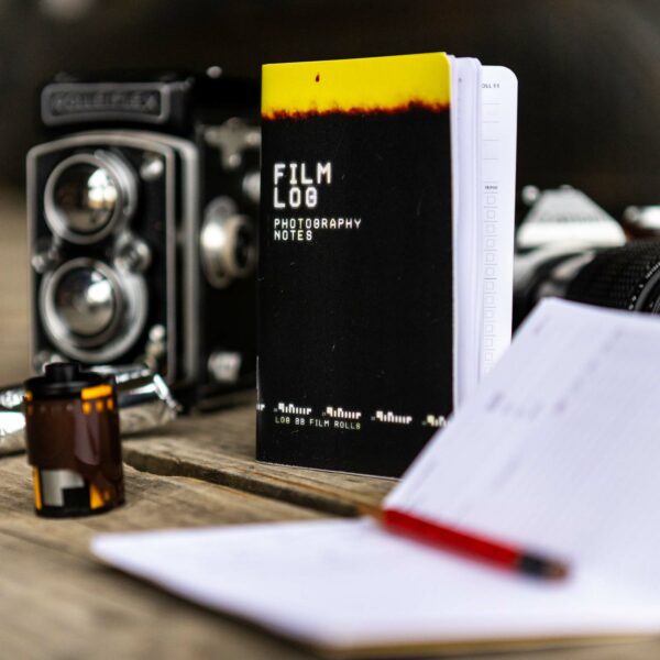 Film Log Photography Notes sits among a Rolleiflex camera, a roll of 35mm film, and a roll of 120 film